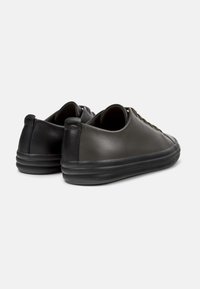 Schwarze und dunkelgrüne Leder-Sneaker mit glatter Textur, runder Form und kontrastierenden, geschichteten Gummisohlen; minimalistisch gestaltete Schnürung.