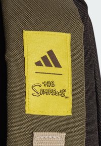 Pezzo di tessuto marrone e giallo con il logo Adidas e il testo "I Simpson", cucito su uno sfondo testurizzato verde e nero.