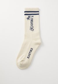 Strikkede sokker i cremefarve med ribbet tekstur, der har blå striber og "KAOTIKO" logo broderet på siden.