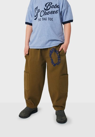 Maglietta grafica blu con maniche corte. Pantaloni cargo larghi color verde oliva con tasche laterali e testo blu del logo. Scarpe nere.