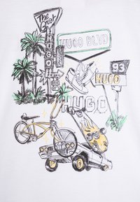 Camiseta gráfica con ilustraciones en tinta negra y verde de un coche vintage, una bicicleta, palmeras y señalización, sobre un fondo de tela blanca.