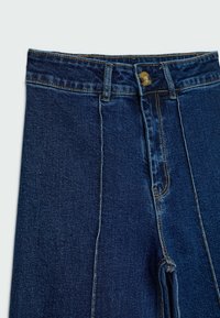 Jeans de mezclilla en azul oscuro con cintura alta, que cuentan con un cierre de botón y costuras amarillas en contraste a lo largo de las costuras y los bolsillos.