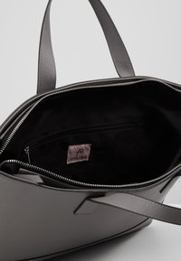 Bolso tote gris hecho de material texturizado, con cierre de cremallera, asas dobles y un interior negro con un pequeño bolsillo con cremallera.