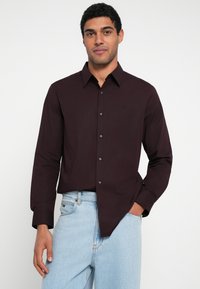 Sötét bordó, gombos, hosszú ujjú ing, hegyes gallérral és fekete gombokkal, világoskék farmernadrággal párosítva.