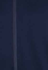 Giacca zip-up blu navy realizzata in tessuto liscio, con una zip centrale e cuciture rinforzate lungo la cucitura.