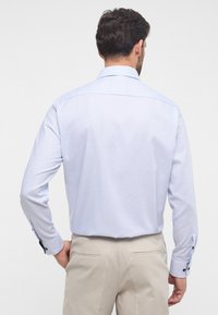 Lichtblauw, gestructureerd shirt met lange mouwen, knoopdetails op de manchetten en een klassieke kraag, gedragen met een beige broek.