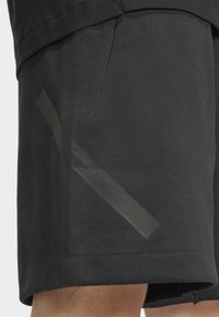 Melnas šortus, izgatavotus no mīksta auduma, ar sānu kabatu un izteiksmīgu melnu gumijotu akcentu kreisajā kājā.