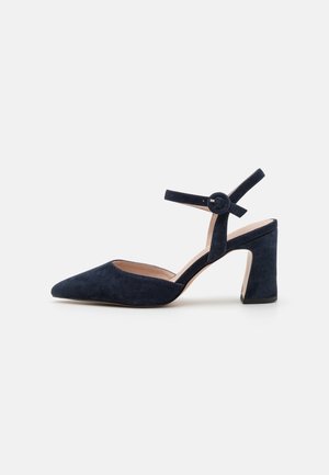 Chaussure habillée femme en daim bleu marine avec bout pointu, talon bloc et bride à la cheville avec boucle sur fond blanc.