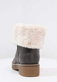 Botte noire à cheville avec une semelle épaisse marron et un large revers en fausse fourrure beige replié sur le dessus.