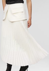 White pleated skirt with a fitted waistband and side pockets. The fabric is smooth, with pronounced vertical folds, extending to mid-calf.