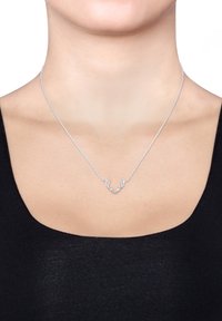 Sølvsmykke med et gevirdesign, delikat kæde og et minimalistisk udtryk. Båret på en halslinje med en sort bluse.