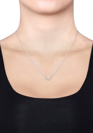 Sølvsmykke med et gevirdesign, delikat kæde og et minimalistisk udtryk. Båret på en halslinje med en sort bluse.