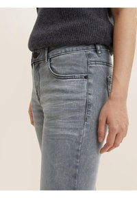 Jeans de mezclilla gris claro con un diseño ajustado, que cuentan con bolsillos estándar, costuras visibles y un ligero desgastado para aportar textura.