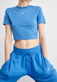 Blå kortärmad t-shirt och blå träningsbyxor, båda gjorda av mjukt tyg. T-shirten har en vit Nike-logotyp; byxorna har ett elastiskt midjeband och snörning.