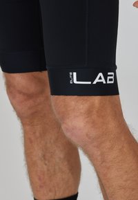 Pantaloni sportivi neri con una vestibilità aderente. Presentano un logo bianco "ELITE LAB" sull'orlo e cuciture flatlock per il massimo comfort. Texture liscia.