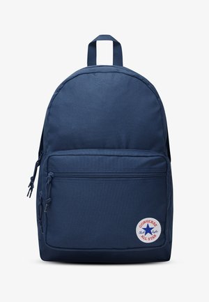 Tmavomodrý batoh Converse s predným vreckom na zips a okrúhlym nášivkom s logom Chuck Taylor All Star v pravom dolnom rohu.