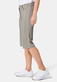 Knee-lange, lichtgrijze shorts met subtiele verticale strepen, een comfortabele elastische tailleband en zijzakken. Draagt witte sneakers.