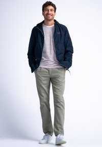 Námornícká lehká bunda s kapucí, pod ní pruhovaná růžová košile, světle šedé kalhoty a bílé tenisky. Bunda má kapsy na zip.