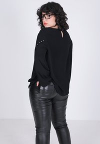 Zwarte langemouwen top met een keyhole detail op de rug en studaccenten op de schouders, gecombineerd met zwarte leren look broeken met een glanzende afwerking.