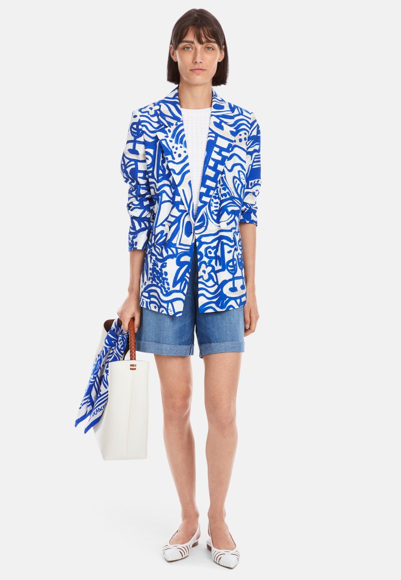 Blazer mit blau-weißem Muster, aus gewebtem Stoff, über einem weißen Oberteil getragen, kombiniert mit Jeansshorts, einer weißen Handtasche und gestreiften Ballerinas.