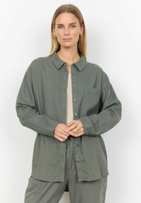 Olivgrünes Langarmhemd mit Knopfleiste, Kragen und Brusttasche. Hergestellt aus weichem Stoff, mit lockerer Passform und geknöpften Ärmeln.