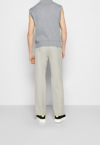 Top sin mangas de rayas gris, pantalones anchos beige y zapatillas negras con acentos neón, vistas desde atrás.