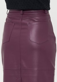 Lilla skinnskjørt med glatt tekstur, midtlengde-design og to baklommer. Sømdetaljer gir et skreddersydd utseende.