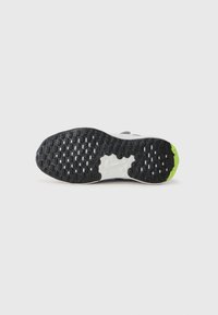 Semelle de chaussure de sport, avec un dessous en caoutchouc noir accentué de petites touches vertes, surface texturée, et une semelle intermédiaire blanche avec un détail de logo.