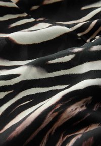 Zwart-witte stof met een zebra-print patroon; zachte textuur; abstracte golvende vormen; variërende tinten zwart, crème en bruine accenten.