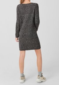 Knitted sweater dress in dark gray with a textured pattern, long sleeves, a rounded neckline, and mid-thigh length. Worn with light sneakers.