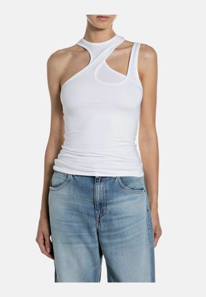 Donna che indossa un top bianco asimmetrico senza maniche con ritagli abbinato a jeans azzurri a vita alta su sfondo bianco.