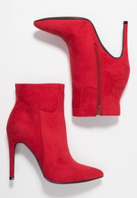 Stivaletti alla caviglia in suede rosso con punta affusolata e tacco a stiletto. Presentano una cerniera laterale e una texture liscia per un aspetto elegante.