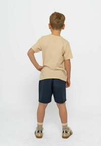 Bežové bavlněné tričko, námořnické šortky, béžové pruhované ponožky a hnědé sandály. Pohled zezadu, který ukazuje jednoduchý design a pohodlný střih.