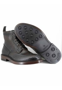 Stivali in pelle marrone scuro con design brogue, caratterizzati da una punta tondeggiante e perforazioni decorative. La suola in gomma presenta un motivo di battistrada circolare.