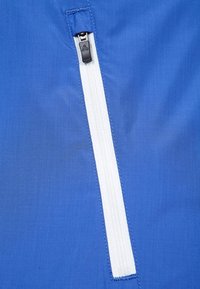 Blått tyg med en vit dragkedja och en svart dragtab. Texturen verkar slät med en subtil glans och rena sömnadsdetaljer.