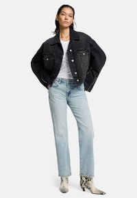 Przesadzona czarna kurtka dżinsowa z przednimi kieszeniami i srebrnymi guzikami, zestawiona z jasnoniebieskimi dżinsami typu straight-leg i wzorzystymi botkami za kostkę.