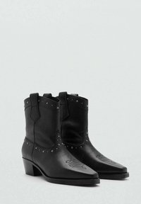 Zwarte leren cowboylaarzen met puntige neuzen, voorzien van zilveren studs rond de enkel en gegraveerde details op de schacht. Lage blokhak.