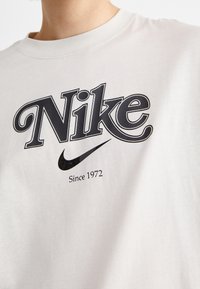 Světle šedé bavlněné tričko s velkým černým logem Nike a textem "Od 1972" pod ním, kulatý výstřih, krátké rukávy.
