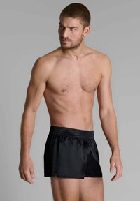 Shorts de bain noirs avec taille élastique, dotés d'une texture lisse et brillante, et de fentes latérales pour une aisance de mouvement. Design à jambes courtes.