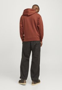 Felpa con cappuccio bordeaux dal taglio rilassato, abbinata a pantaloni grigi scuri a vestibilità morbida e scarpe marroni. Il tessuto sembra morbido e texturizzato.