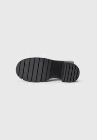 Black rubber sole with a ridged pattern for traction. Smooth edges and sturdy construction, providing durability and support.