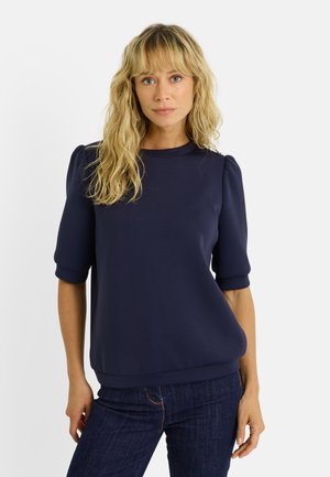 Pull bleu marine avec des manches courtes bouffantes, un col rond et une coupe décontractée. Fabriqué à partir d'un tissu doux, sans motifs ni accents visibles.
