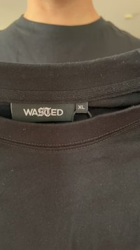 Schwarzes Baumwoll-T-Shirt mit Rundhalsausschnitt. Das Etikett trägt den Aufdruck "WASTED" in Weiß, Größe XL, mit glatter Textur und ohne sichtbare Muster.