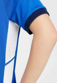 Camiseta atlética azul con cuello marino, que presenta paneles de malla blanca transpirable y un ajuste estructurado, destacando un diseño elegante.