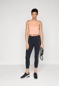 Rožinė trumpa sportinė liemenė, tamsiai mėlynos tamprės su baltomis šoninėmis juostomis ir juodi sportbačiai. Lygus audinys, aptemptas dizainas ir laisvas siluetas.