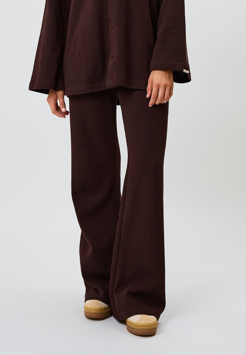 Ensemble en top en tricot côtelé couleur cacao et pantalon évasé, présentant une coupe décontractée, de grands boutons et des accents texturés contrastants. Des chaussures à plateforme beige viennent compléter le look.