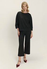 Haut en tricot noir avec un col rond et des manches trois-quarts, assorti à un pantalon noir à larges jambes. Des escarpins bordeaux à bout pointu complètent le look.