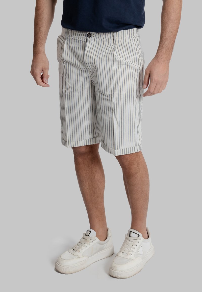 Pantaloni corti a righe da uomo in un beige chiaro con righe verticali blu, dotati di chiusura con bottone, tasche e una vestibilità casual. Indossati con scarpe da ginnastica bianche.