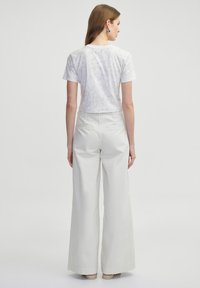Un crop top blanc à manches courtes avec une texture légèrement marbrée, associé à un pantalon large taille haute de couleur beige clair, comprenant des poches arrières.