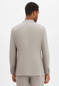 Lichtgrijs op maat gemaakt colbert van een gestructureerde stof, slim fit, met ingezette revers en knoopdetails aan de mouwen. De achterkant toont strakke lijnen en een lichte ventilatie.